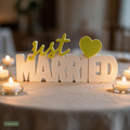 Deko-Schriftzug Just Married auf Hochzeitstafel umgeben von brennenden Teelichtern, KI-generiert